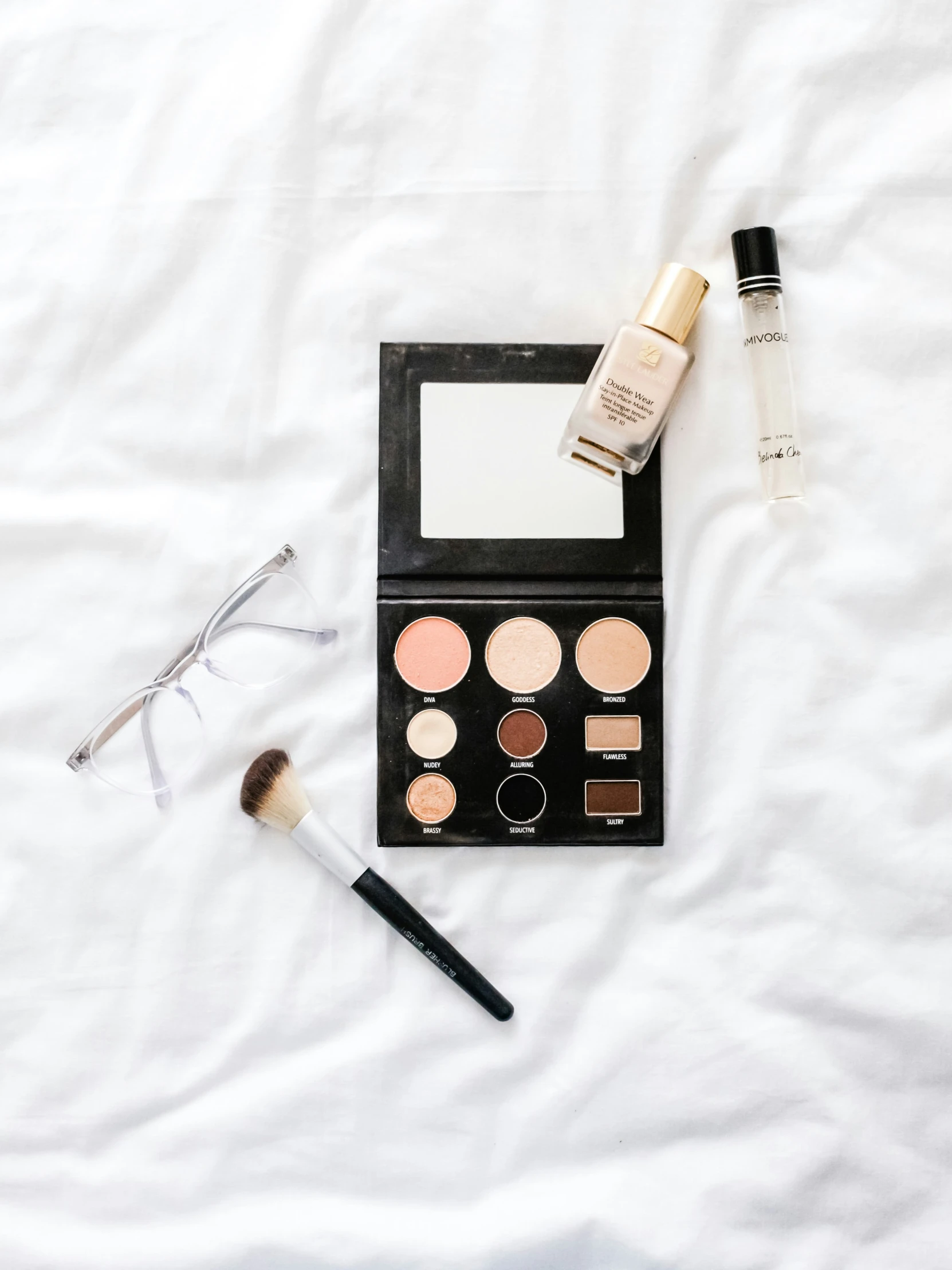 an open notebook, cosmetics, eyeliners and a pair of eye glasses on a white sheet