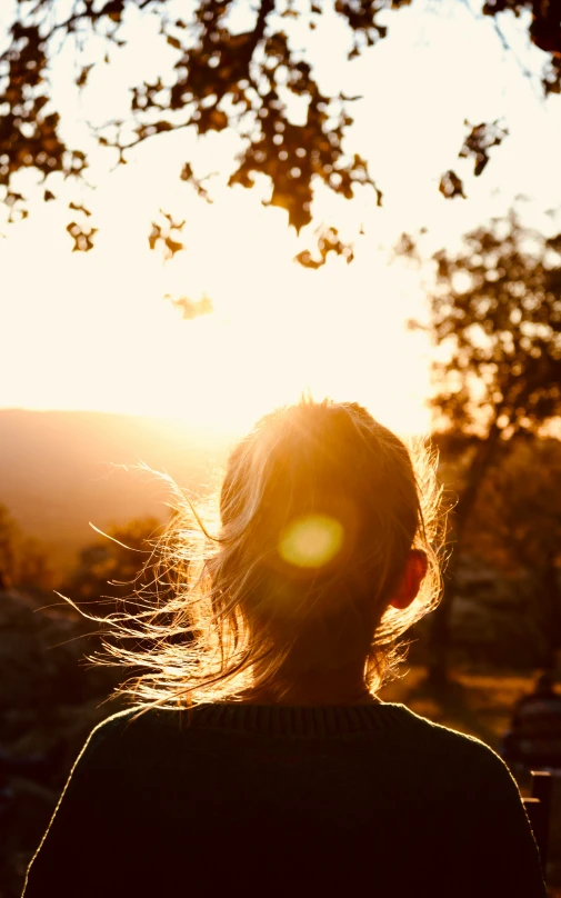 a woman is looking into the distance while the sun sets