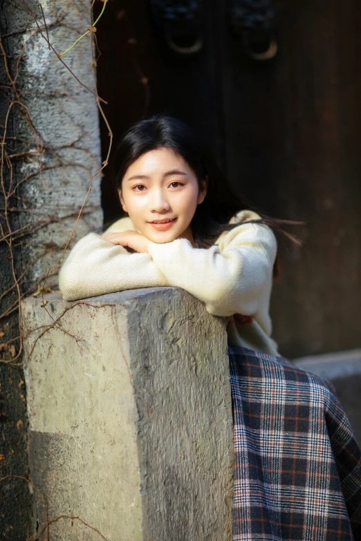 an asian woman leaning against a concrete wall