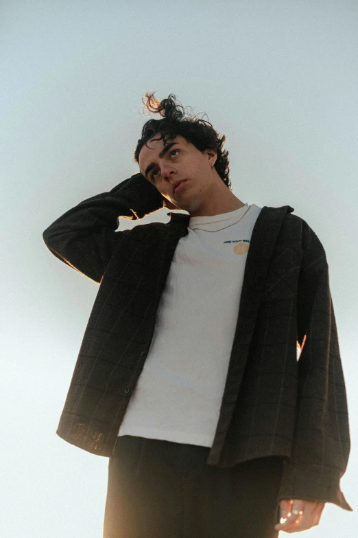 man in black sweater standing near wall with one hand on his ear