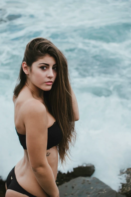 a woman in black bikini standing on top of a rocky shoreline