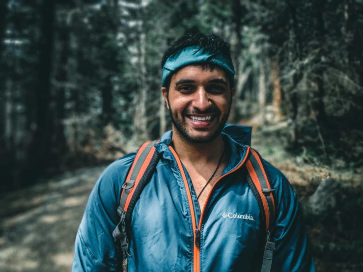 a smiling man stands in the middle of a wooded trail