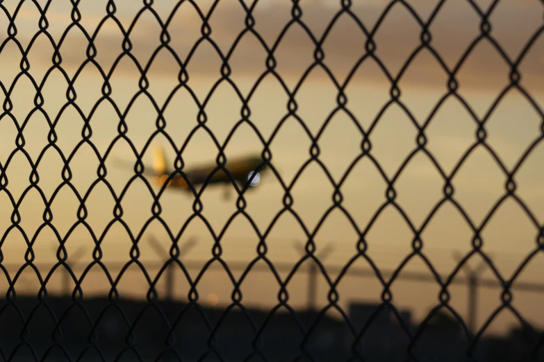 a plane is seen through the chain link fence