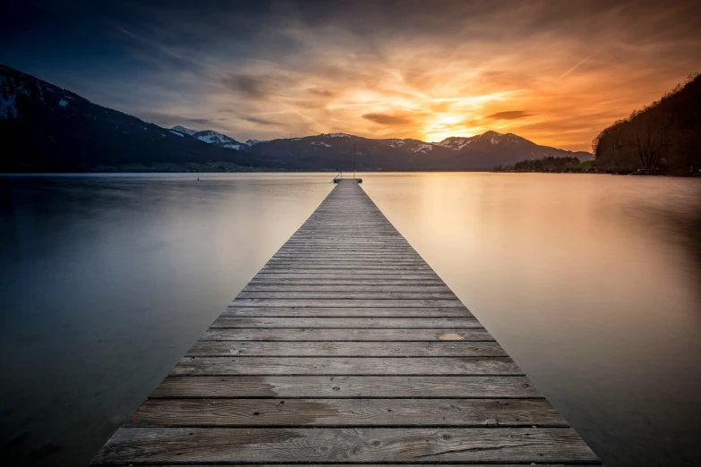 a wooden pier on the water with a mountain range in the background