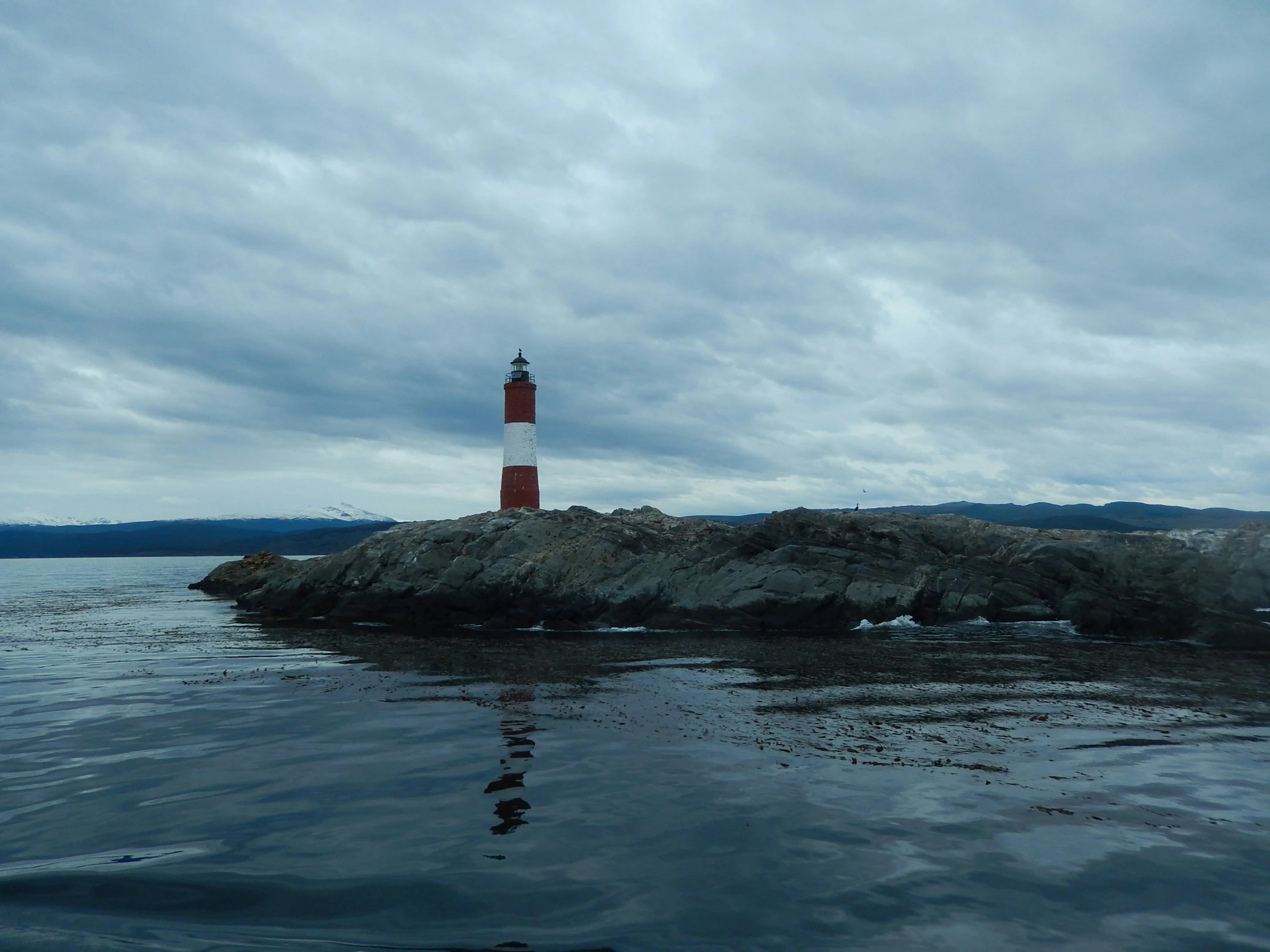 a red light house sitting on top of a rocky island