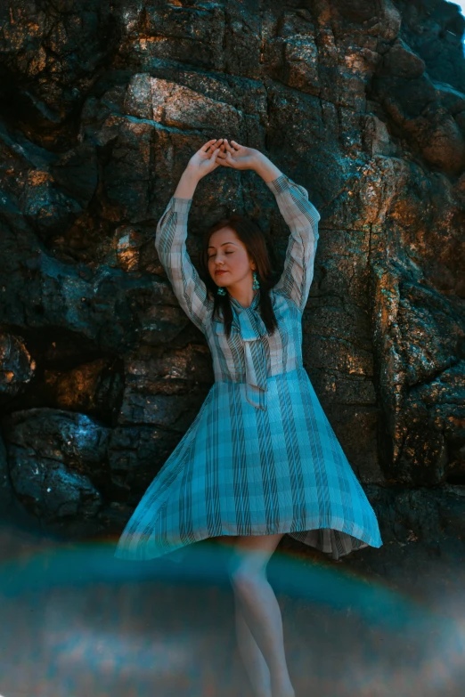 a girl standing near a rock holding her arms above her head