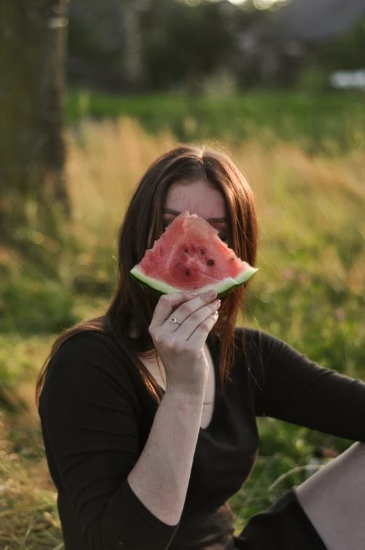 a lady eating a piece of watermelon on the grass