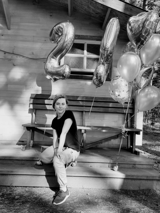 woman sitting on a bench in front of a number of balloons