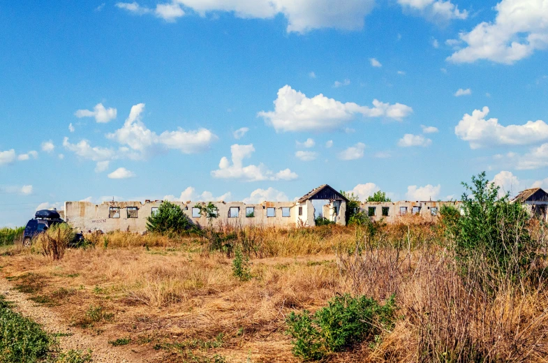 an abandoned building sits near a field on the outskirts