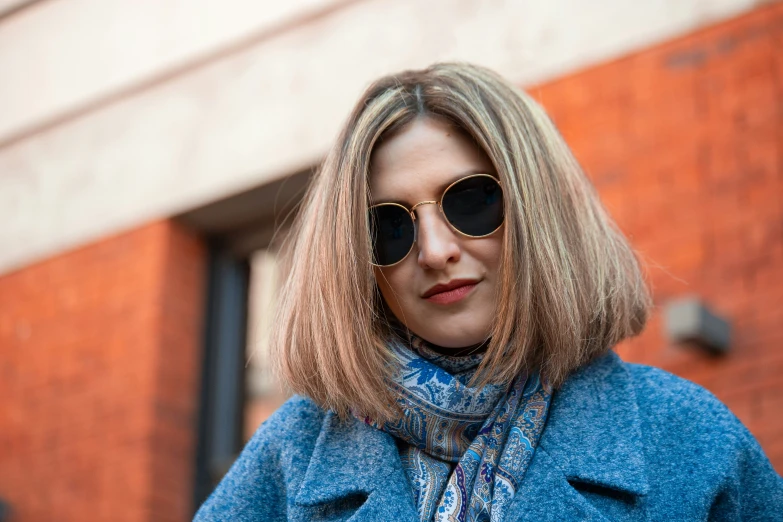 a blonde woman in a coat, scarf and sunglasses