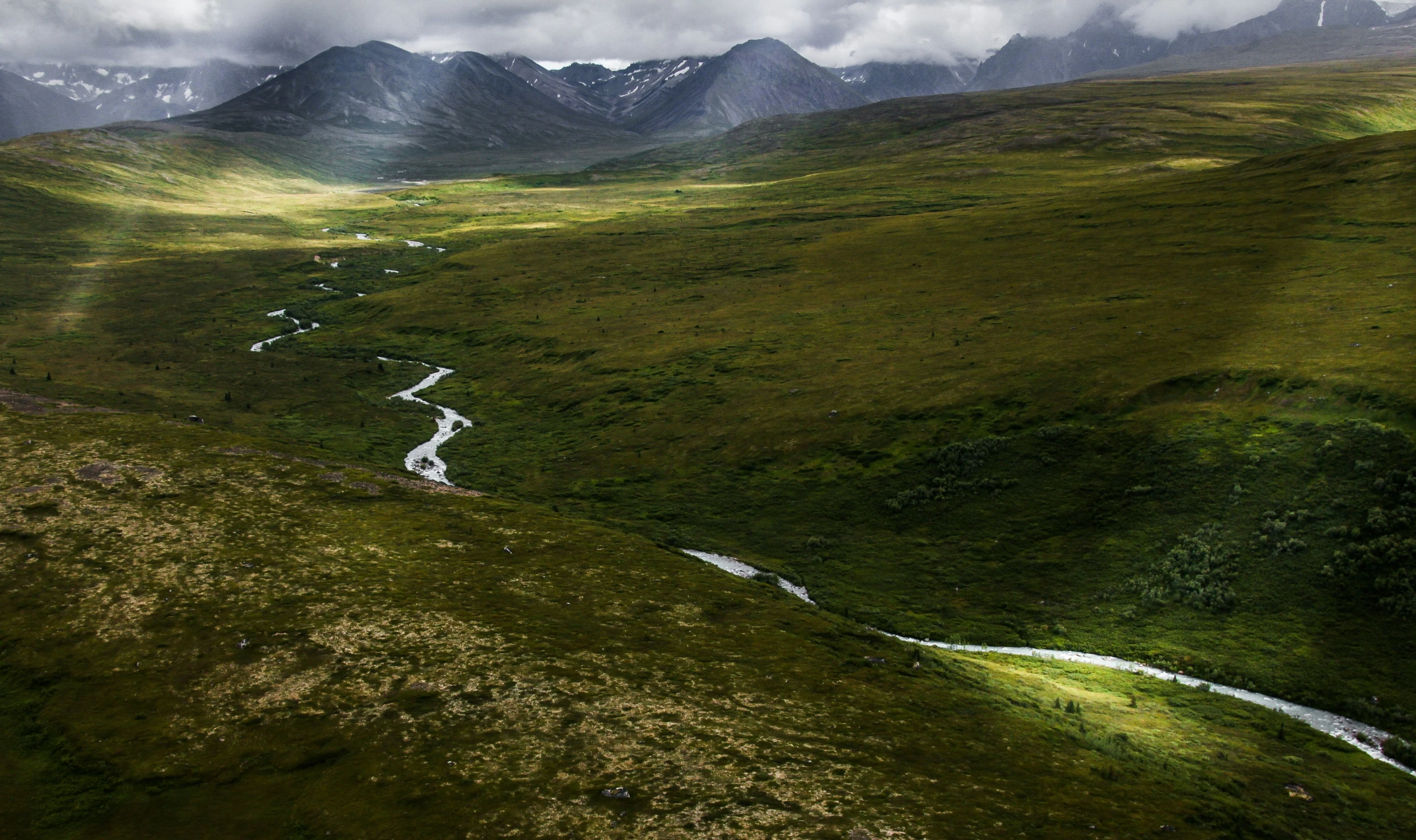 a very big grassy hillside with a river running by it