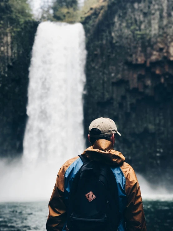 a man wearing a baseball cap looking at a waterfall