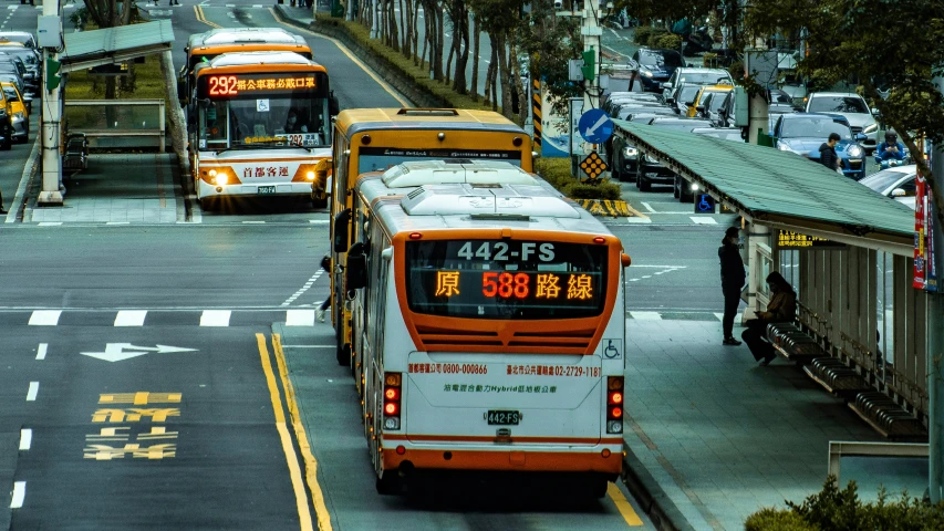 two buses on the street and some people are standing in the background