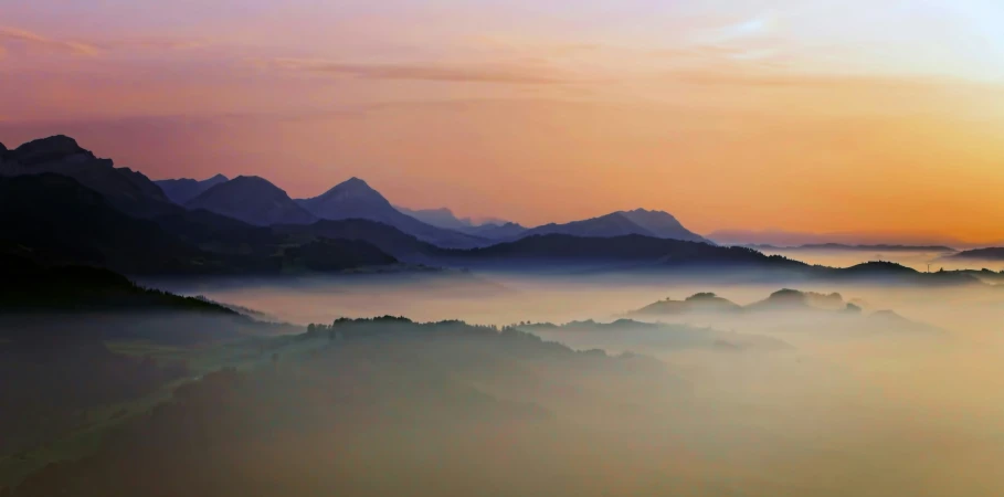 the mountains are covered in fog as the sun sets