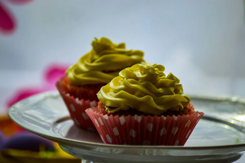 a pair of cupcakes with yellow frosting on a small cake plate