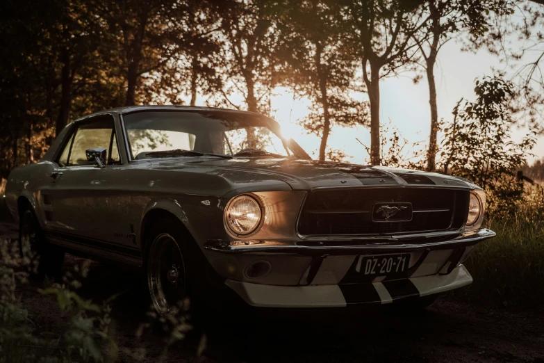 a classic mustang car is on the dirt with trees and grass behind it