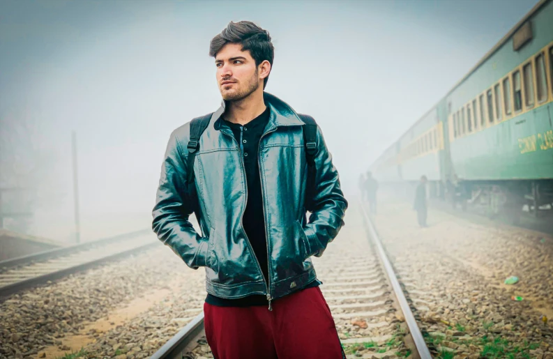the man is posing near a railroad track