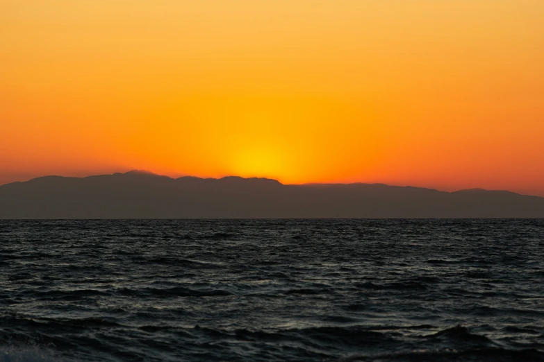 the sun sets behind a silhouetted island on a calm body of water