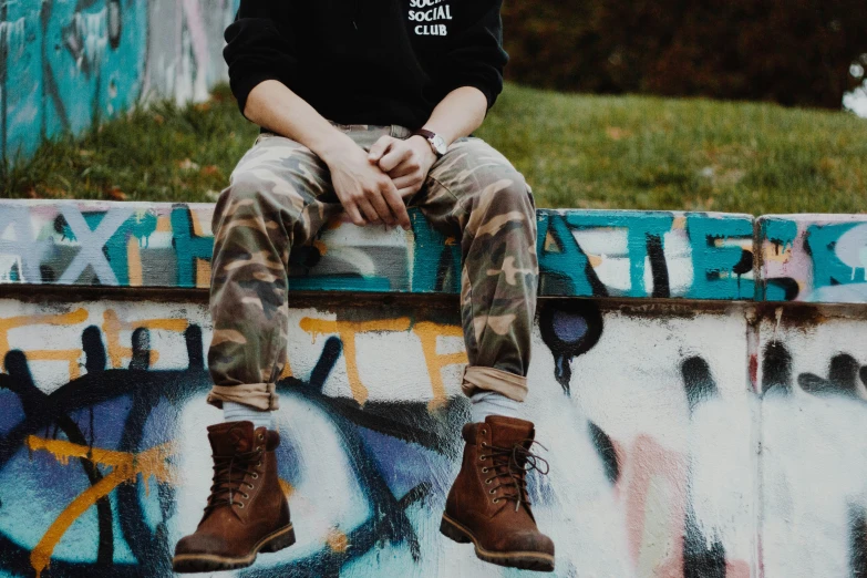 young man sitting on cement slab with graffiti covered wall