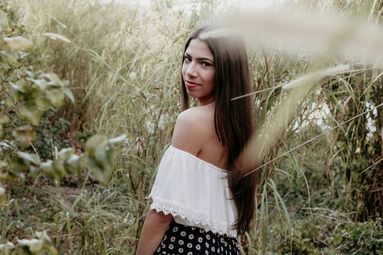 a woman standing in tall grass by some bushes