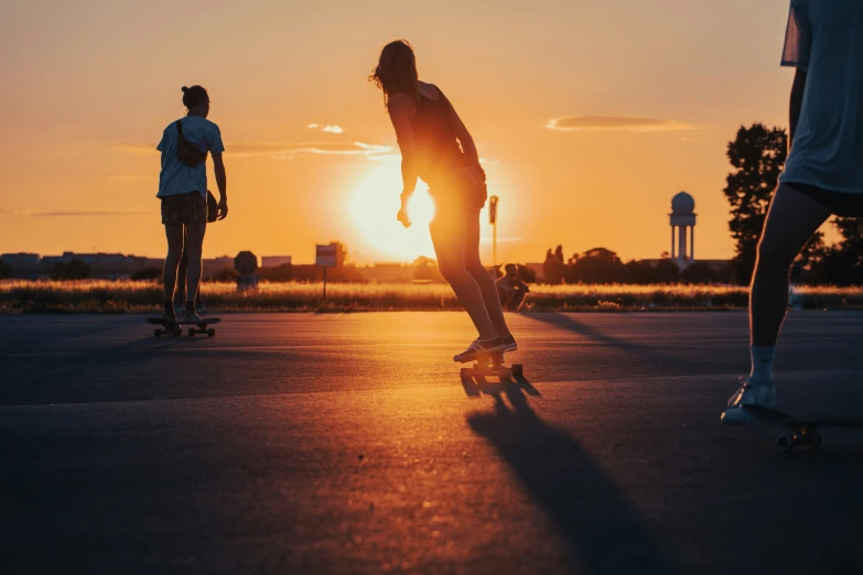 two people skateboard along an asphalt path in the middle of sunset