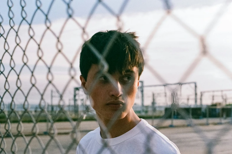 man in white shirt standing behind chain link fence