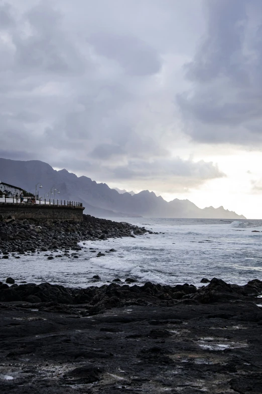 a dark and cloudy beach with mountains in the distance