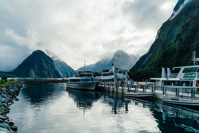 boats are lined up along the shore as mountains and clouds loom in the background