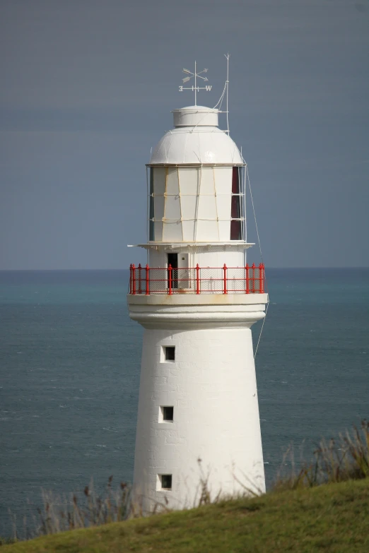 white lighthouse with red railing standing near a body of water