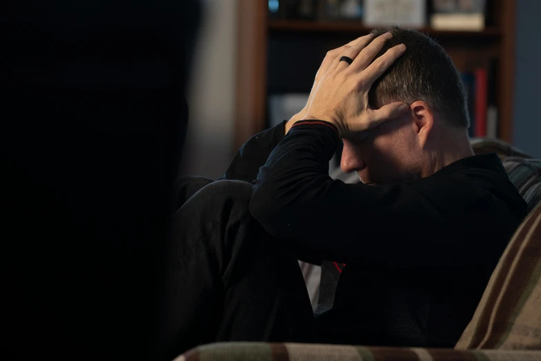 a man holding his head while sitting on a couch