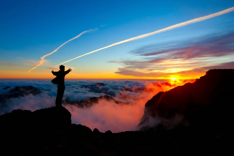 man standing on the edge of a cliff, overlooking clouds