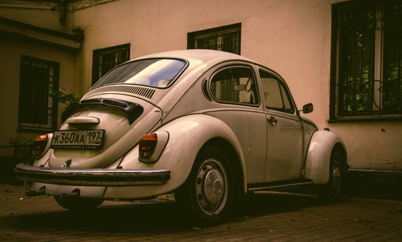 old vw bug parked on cobblestone with windows on an urban building