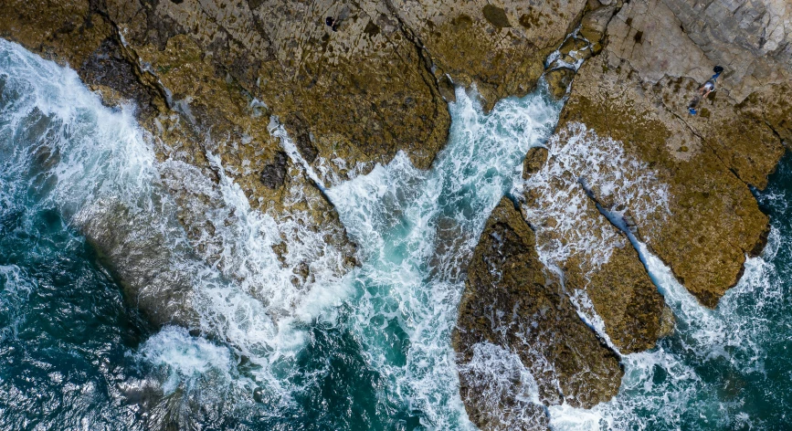 two swimmers wading in the ocean near some rocks