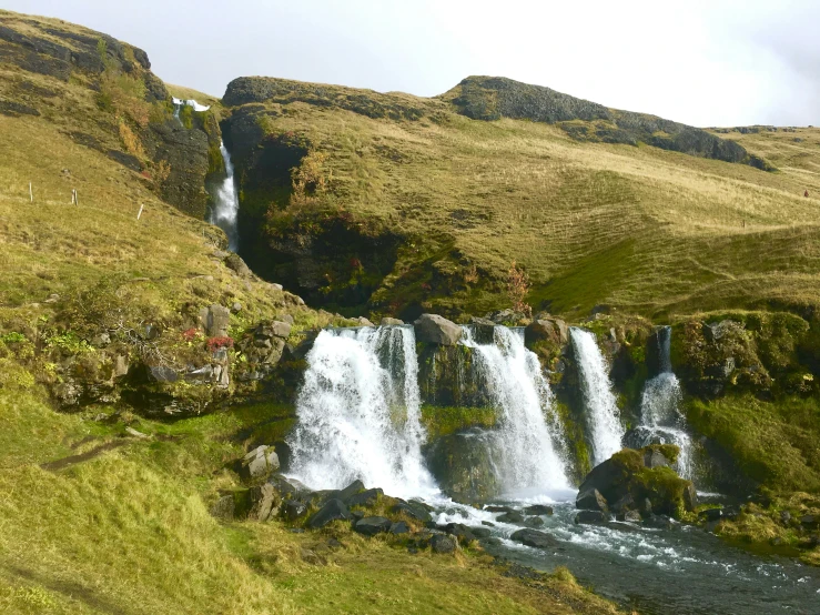 a large waterfall and small grassy hill with a blue pickup