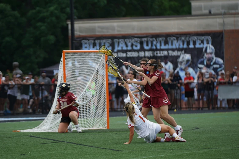 girls in maroon uniforms fight for control of the ball while playing lacrosse