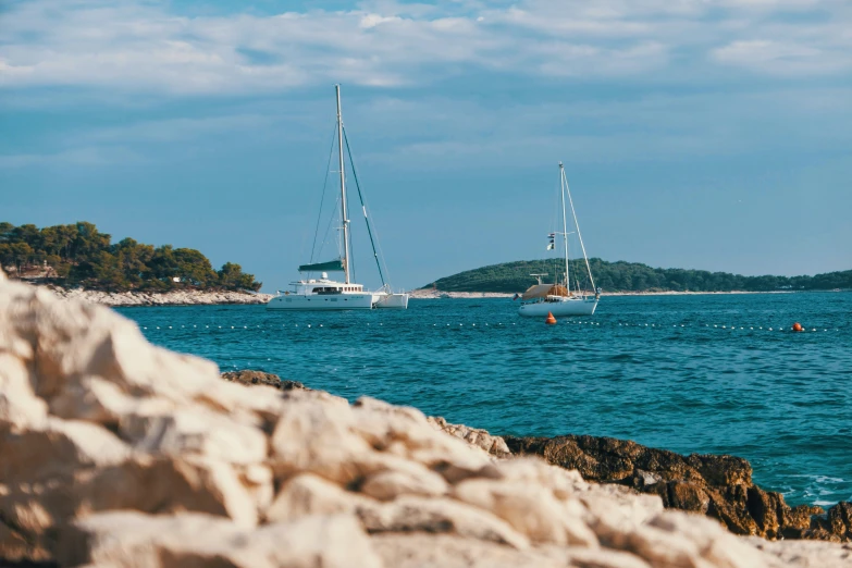 two sail boats are out in the ocean near some rocks