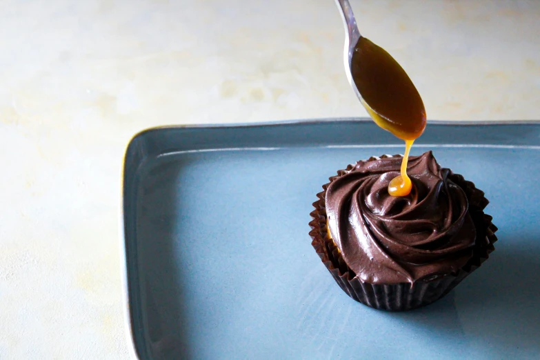 the spoon is drizzling er on a cupcake