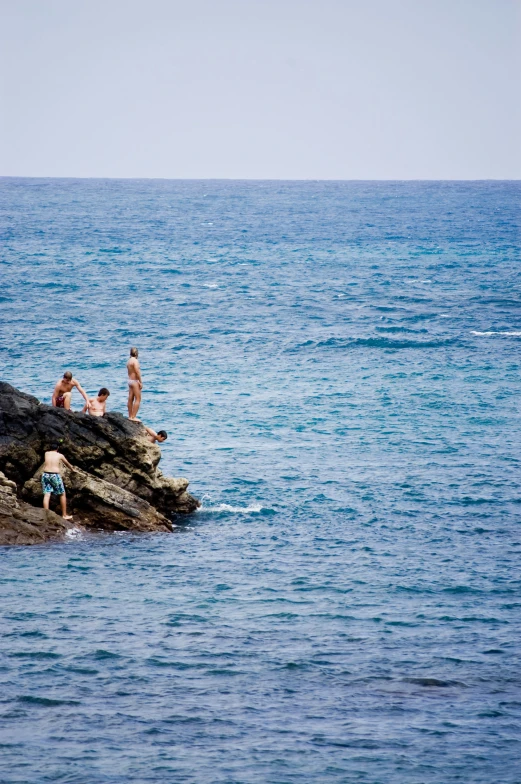 three people in swimsuits are lounging on rocks and water