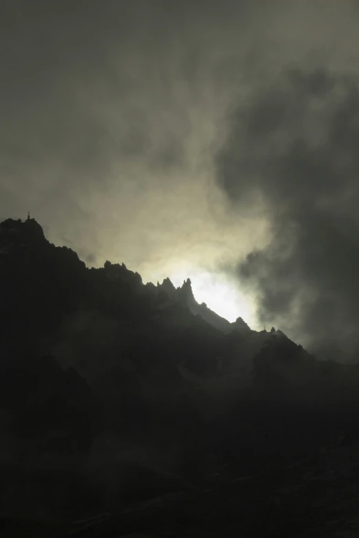 sun shining through dark clouds over mountains and hills