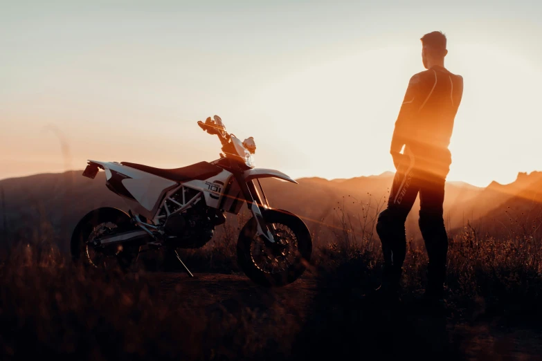 a person stands next to a dirt bike at sunset