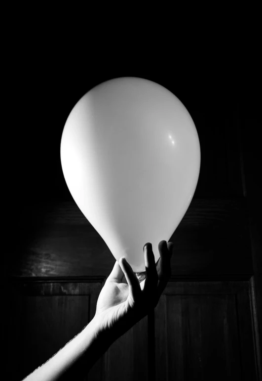 a person holds a white balloon to a dark room