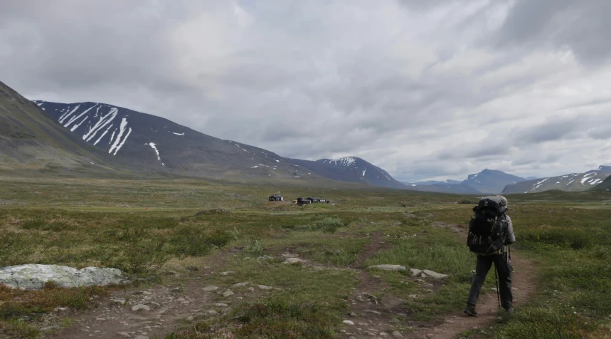 a hiker walks up a path past mountains and grassy fields