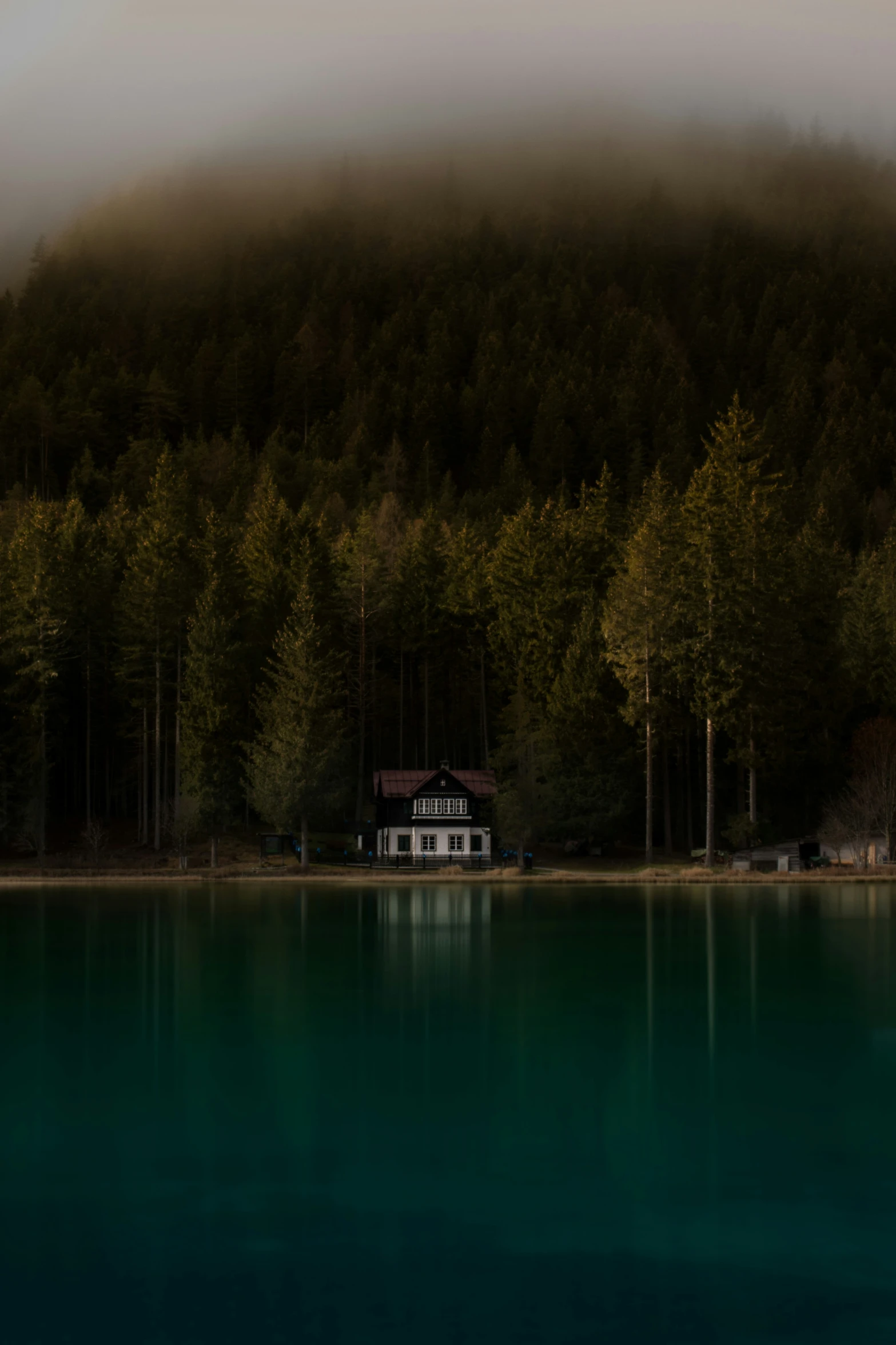 fog in the mountains surrounding the water and a house on the lake