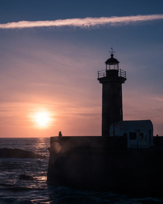 the sun rises over a lighthouse at sunset