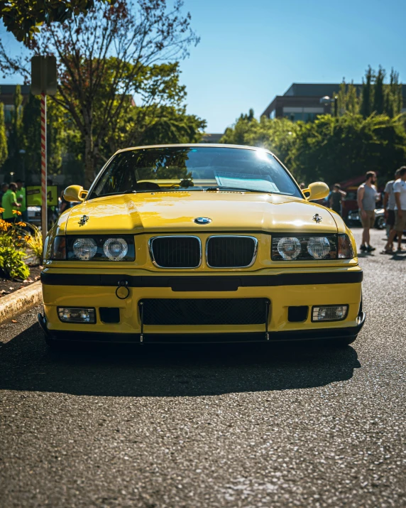 a yellow car is on the road near a crowd