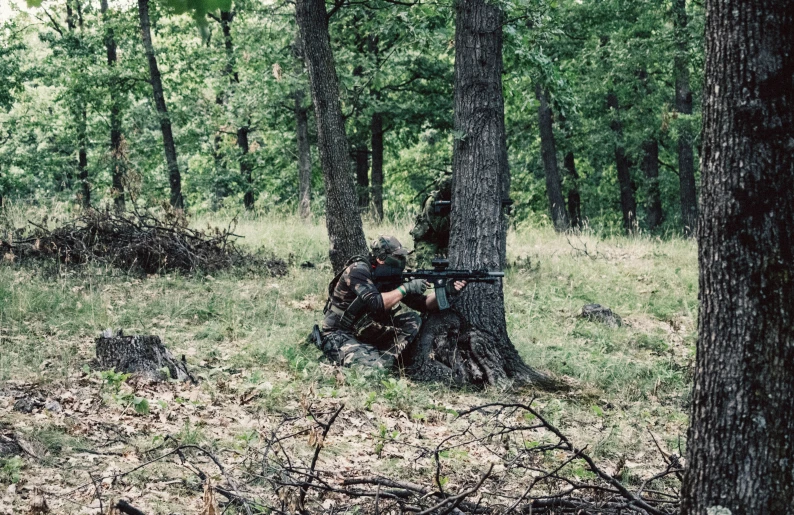 a soldier is crouched in the woods by a tree