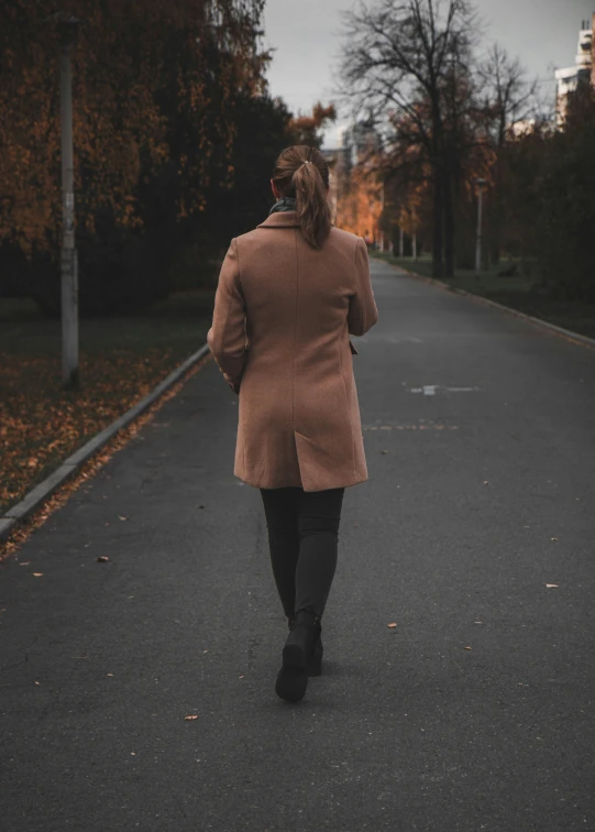 woman in brown coat walking down street near house