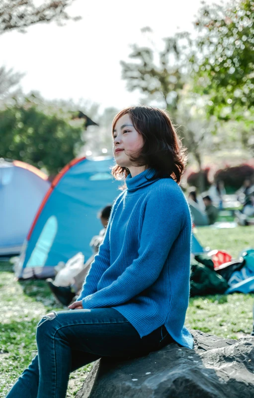 a woman is sitting on a rock with tents in the background