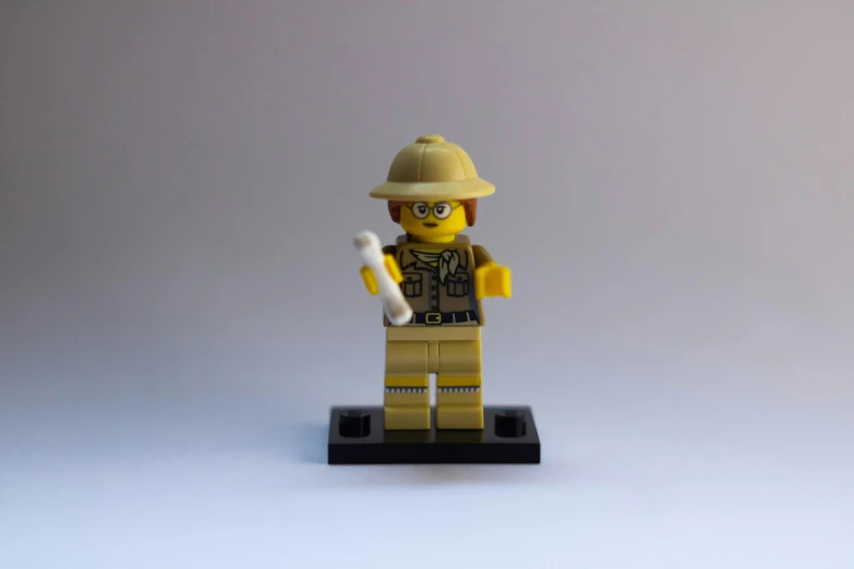 a lego man holding an electronic device and wearing a hat