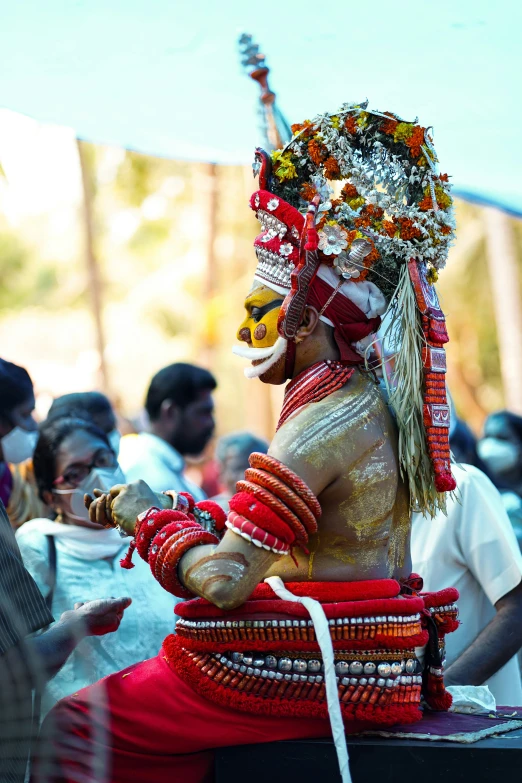 man dressed in elaborately painted head dress sitting on a small wooden platform